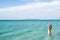 Back of beautiful woman wearing blue bikini standing in the water on Mediterranean sea coast, Cesme, Ilica beach, Turkey