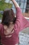 Back of a brunette young lady in a dusky pink top with flared sleeves, waving her arm throwing something