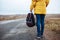 Back closeup view of a female walking the lonely road with a backpack in her hand. Young woman travels during winter or autumn