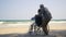 Back elderly woman disabled sitting in wheelchair and husband is a wheelchair user on the beach