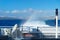 Back of ferry with rainbow from splashing water with blurred view on Santorini cliffs, Greece