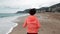 Back follow shot of young woman is running on beach in the morning. Sporty motivated female is jogging on seashore. Female tourist