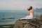 Back of girl in wedding dress sitting on rocks in mountains and looking to fjord