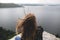 Back of hipster girl sitting on top of rock mountain with beautiful view on river. Young tourist woman with windy hair relaxing on