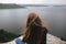 Back of hipster girl sitting on top of rock mountain with beautiful view on river. Young tourist woman with windy hair relaxing on