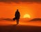 Back lit silhouette of solitary person walking towards the setting sun on the horizon through barren desert landscape