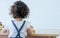 Back of little caucasian adorable curly hair lonely girl wearing white casual clothes, playing toys alone on wooden table at cozy