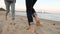 Back low angle view of romantic couple feet running on sand holding hands on beach near sea in slow motion. Boyfriend