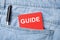 The back pocket of blue jeans contains a white pen and a white red card with the text guide