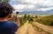 Back or rear view of a male hiker in casual clothes stands in a mountain trail with a sport camera on a stabilizer gimbal and