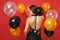 Back rear view of tender young woman in little black dress celebrating on red background air balloons. St. Valentine`s