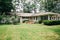 Back Rearview of exterior white cream brick 1950`s house with black shutters and a large lawn lot