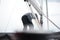 Back of an sailor man setting sail, trimming the mainsail on deck of a sailboat