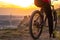 Back shot of mountain biker at sunset sitting on a modern off-road bike on the hill behind the city.