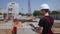 Back Shot of Professional Construction Worker Wearing Hard Hat Holds Tablet Computer, Standing in Modern Industrial