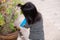 Back side of girl watering the plants with blue plastic bowl. Children wear black and white striped shirts.