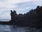 Back side of older man, local fisherman in hat standing on the edge of lava rock cliff with fishing rod at coast of