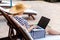 Back side portrait of beautiful young adult freelancer woman in hat and dress is sitting on cozy sunbed and using laptop computer