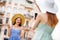 Back side portrait of person with red hair photographing her buddy making v-signs wearing dress in town