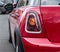 The back and side of a red Mini Cooper. One back headlight of a red Mini Cooper parked on the street.