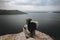 Back of stylish hipster girl sitting on top of rock mountain with beautiful view on river. Young tourist woman with windy hair