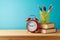 Back to school background with pencils, books and alarm clock on wooden table over blue background