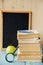 Back to school background on wooden table and blackboard on a background. Books, pencils, alarm clock and apple on desk. Apple on