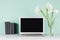 Back to school background - workplace with blank notebook monitor, black books and white fresh flowers in light green mint menthe.