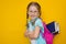 Back to school. Beautiful little girl in glasses and with pigtails with books in a school backpack smiling looking at