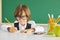 Back to school. Clever boy a schoolboy writes with a pencil while sitting at a table on the background of the school