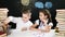 Back to school concept. Children sit at a desk with heaps of books and a blackboard with kids drawings behind them. Boy