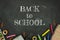 Back to school concept. Top view tationery, notepads, pencils and clips over classroom blackboard with white chalk sign