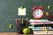 Back to school and education concept with alarm clock, green apple and stationery supplies against blackboard with numbers
