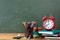 Back to school or education concept with alarm clock, paper notebooks and school supplies against blackboard background.