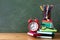 Back to school or education creative concept with red alarm clock, colorful notebooks and school supplies against blackboard