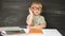 Back to school. Happy smiling pupil in round glasses sitting at the desk. Child raises his hand up in the classroom with