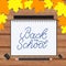 Back to school lettering hand written in a notebook. Wooden texture background and fall leaves. Vector template for advertising