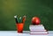 Back to school, orange pencil holder, stack of books on white table with red apple, empty green school board background, education