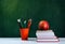 Back to school, orange pencil holder, stack of books on white table with red apple, empty green school board background, education