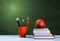 Back to school, orange pencil holder, stack of books on white table with red apple, empty green school board background, education