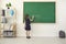 Back to school. Rear view of a schoolgirl in chalk writes on a school chalkboard in class.