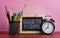 Back to School Text. Blackboard, Alarm Clock and School Stationary in Basket on Wooden Table Pink Background