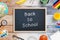 Back to school text on Chalkboard surrounded by stationery, toys, and snack on wooden table