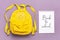 Back to school text on open notepad, education concept. Yellow backpack isolated on violent background. Top view Flat lay