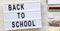 `Back to school` words on a lightbox, accessories for study on a white wooden surface, view from above. Top view, overhead, flat