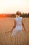 Back veiw on beautiful young woman walking on the rye field at sunset. Happy girl enjoying countryside life. Sunset