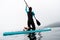 Back view active sportswoman in diving suit floating on stand up paddle at fog sea scenery