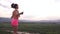 Back view on active young brunette woman jumping with skipping rope on the mountain peak. Green mountain ladscape