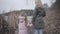 Back view of adult blond woman and little brunette girl standing in autumn bushes in front of lake or river. Caucasian