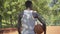 Back view of African American sportsman in white shirt standing with ball on sunny basketball court, turning to camera
